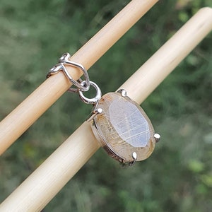 May include: A silver pendant featuring a clear oval-shaped gemstone with gold inclusions. The pendant is attached to a silver chain.