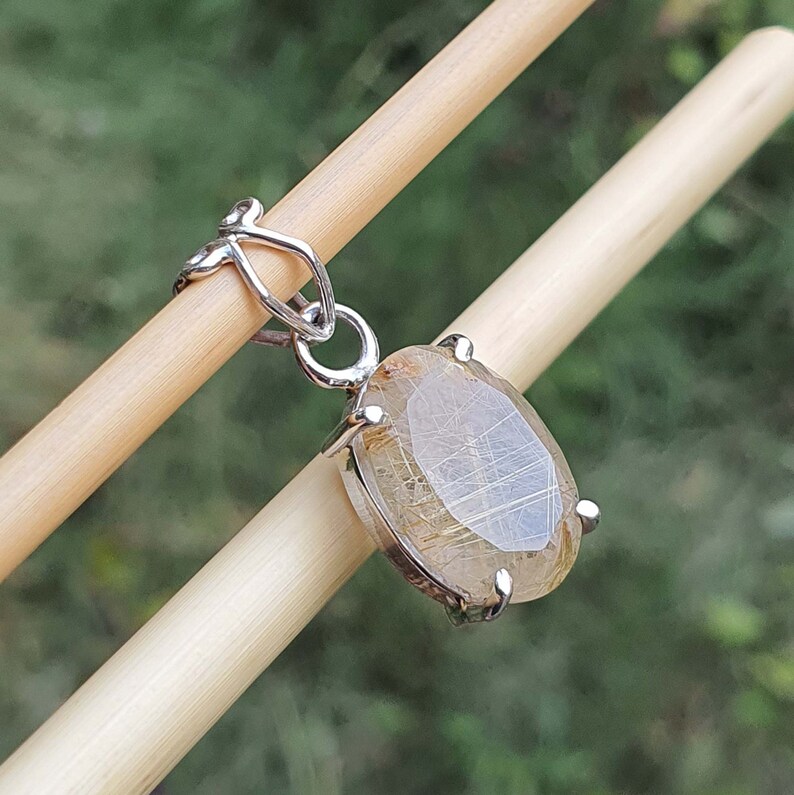 May include: A silver pendant featuring a clear oval-shaped gemstone with gold inclusions. The pendant is attached to a silver chain.