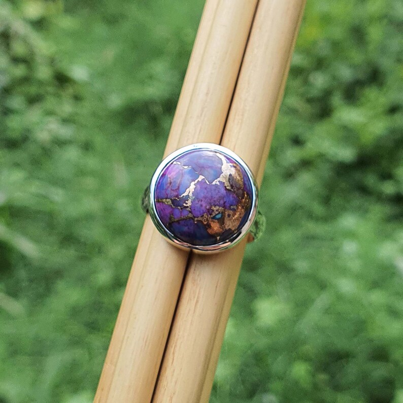 May include: A silver ring with a round purple and copper turquoise stone.