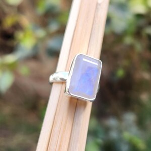 K&ouml;nnte beinhalten: Ein silberner Ring mit einem rechteckigen, schillernden Mondstein. Der Stein hat eine blaue und wei&szlig;e Farbe.