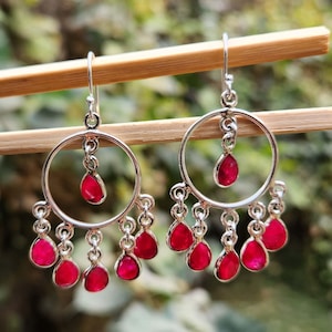May include: Silver hoop earrings with dangling pink gemstones. The earrings have a circular design with multiple pink stones hanging from the bottom.