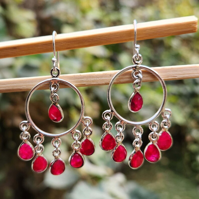May include: Silver hoop earrings with dangling pink gemstones. The earrings have a circular design with multiple pink stones hanging from the bottom.