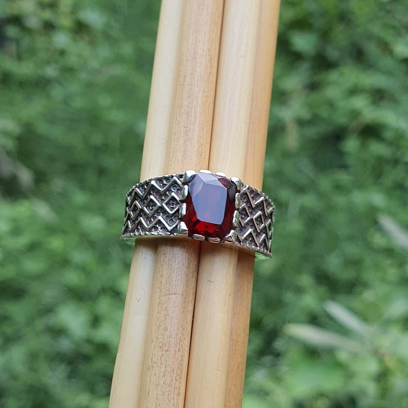 May include: A silver ring with a geometric design and a red gemstone.