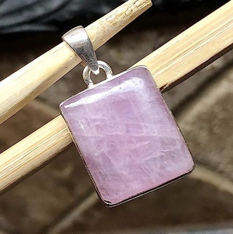 Peut inclure: Un pendentif en argent avec une pierre pr&eacute;cieuse rectangulaire rose clair. Le pendentif est suspendu &agrave; un b&acirc;ton en bois.