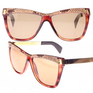 May include: A pair of brown tortoiseshell sunglasses with a snakeskin pattern on the frame. The sunglasses have a gold metal accent on the arms.