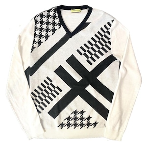 Puede incluir: Jersey blanco de manga larga con un patrón geométrico en blanco y negro. El jersey tiene cuello en V y el texto "VERSACE JEANS" es visible en el cuello.