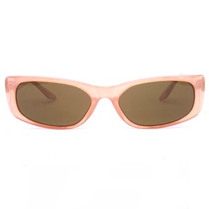 Puede incluir: Gafas de sol rosa pálido con lentes rectangulares y montura a juego. Las lentes son de color marrón oscuro. Las gafas de sol están sobre un fondo blanco.