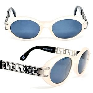May include: White oval sunglasses with a silver chain detail and a black Versace logo on the side. The sunglasses have blue lenses.