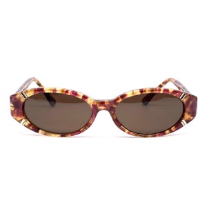 May include: Oval-shaped sunglasses with a tortoiseshell pattern in shades of brown and red. The frames have a gold accent on the edges.