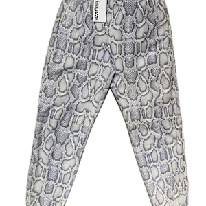 May include: Light grey and white snake print joggers with an elasticated waistband and cuffs. A white tag with the text "kragazze" is attached. The trousers are made of a soft material. The design resembles snakeskin.
