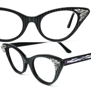 May include: Black cat-eye glasses with a striped pattern and silver accents. The glasses have a vintage style.