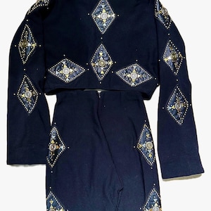 May include: A black two-piece outfit comprising a cropped jacket and a skirt. The jacket and skirt are decorated with diamond-shaped embellishments in gold, silver, and black. The outfit has a vintage or retro aesthetic.