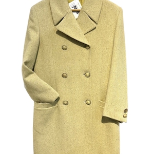 May include: A long, double-breasted coat in a light beige color with a speckled texture. The coat has four large gold buttons down the front and two flap pockets.