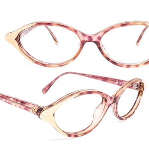 Puede incluir: Un par de gafas ovaladas de color rosa y dorado con un patrón de carey. Las gafas tienen un delicado borde dorado alrededor de los bordes.
