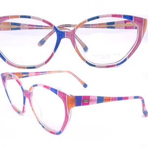 Puede incluir: Un par de gafas coloridas con un patrón a rayas en rosa, azul, naranja y amarillo. Las gafas tienen una forma de ojo de gato y están hechas de plástico. El nombre de la marca "COLLECTION SEDRA" está impreso en la lente derecha.