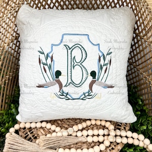 May include: White square pillow with embroidered duck and initial design. The pillow features a quilted pattern and a central emblem with the letter "B", ducks, and reeds. The design includes blue and green accents, with the text "Steele Magnolia Embroidery".