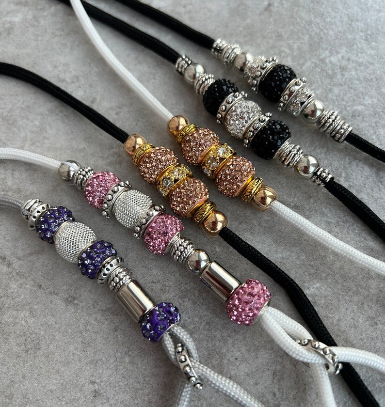 K&ouml;nnte beinhalten: F&uuml;nf verschiedene Hundeleinen mit Juwelenbesatz. Jede Leine hat ein anderes Farbschema, darunter Pink, Lila und Gold. Die Leinen sind aus schwarzem und wei&szlig;em Kordel gefertigt.