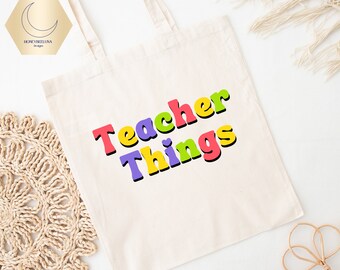 Può includere: Una borsa tote in tela color crema con il testo "Teacher Things" stampato in un carattere retrò audace e multicolore. Le lettere sono colorate in tonalità di rosa, viola, giallo e verde, ciascuna delineata in nero.