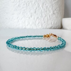 May include: A delicate bracelet made with tiny, light blue crystal beads and a gold clasp.