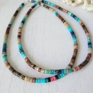 Puede incluir: Dos collares de cuentas con una variedad de colores, incluyendo turquesa, marrón, beige y rojo. Los collares están hechos de pequeñas cuentas redondas. Se exhiben sobre una superficie blanca.