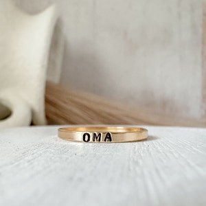 May include: A gold band ring with the word "OMA" engraved in black lettering.