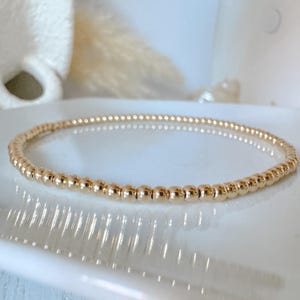 Pode incluir: Um bracelete de contas douradas com um design delicado. O bracelete é feito de pequenas contas redondas que são igualmente espaçadas.