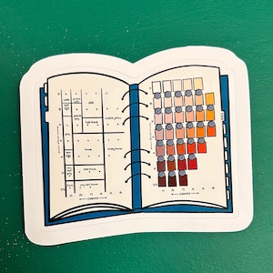 Peut inclure: Un livre de nuancier de couleurs avec une couverture bleue et une reliure spirale. Le nuancier montre une gamme de tons de peau allant du très clair au très foncé. Le nuancier est étiqueté avec les termes "valeur" et "chroma".