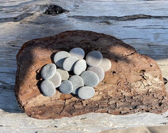 May include: A collection of smooth, gray stones arranged on a piece of weathered driftwood.