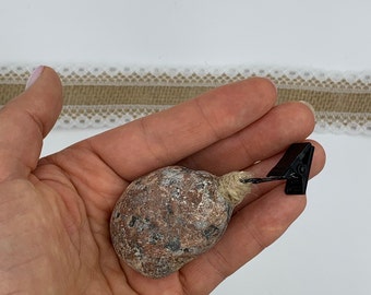 May include: A brown and gray stone with a rough texture is attached to a black clip with a twine string.
