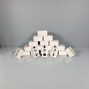 May include: A collection of small, white concrete blocks arranged in a pyramid shape. Some blocks are stacked, while others are scattered around the base. The blocks have a rectangular shape with three hollow openings.