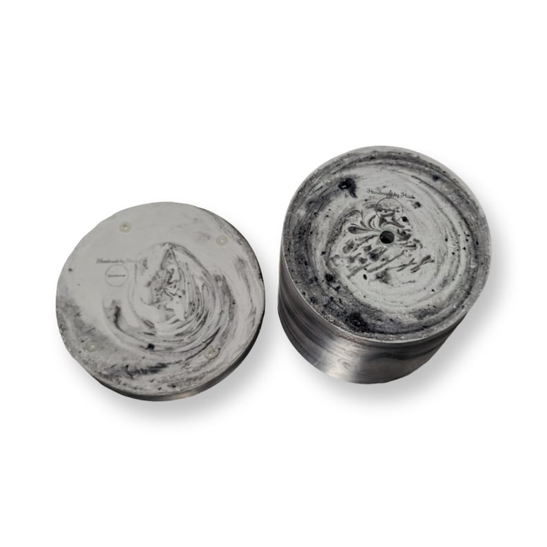 May include: Two round concrete planters with a black and white marbled design. The smaller planter is flat and the larger planter is cylindrical. Both planters have a hole in the centre.