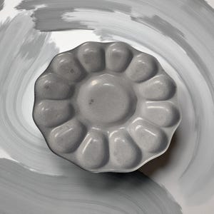 Peut inclure: Une palette de peinture grise en forme de fleur avec plusieurs puits pour mélanger les couleurs. La palette est faite d'un matériau lisse et brillant et repose sur une surface blanche avec des coups de pinceau gris. La palette est conçue pour les artistes et les peintres.