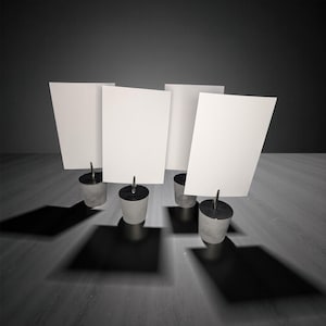 May include: Four concrete and metal card holders with white rectangular cards. The holders have a cylindrical base and a metal clip to hold the cards. The cards are blank and angled.