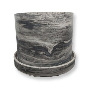 May include: A grey and black marbled ceramic planter with a matching saucer. The planter has a smooth, rounded shape and a subtle swirl pattern.
