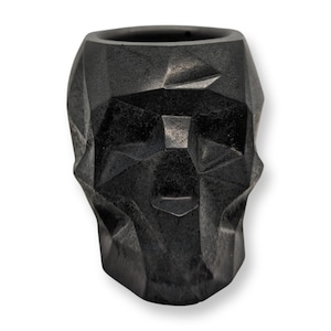May include: A black, geometric skull-shaped container. The container has a textured surface and a wide opening at the top. The design features angular facets, creating a modern, edgy aesthetic. Ideal for home decor or as a unique gift.