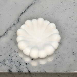 Puede incluir: Un plato de cerámica blanco con un borde festoneado. El plato tiene forma de flor y un acabado liso y brillante.