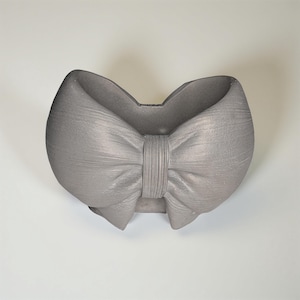 May include: A gray, bow-shaped decorative object. The bow has a textured surface and a central knot detail. The object is likely made of a solid material and is designed to be a decorative accent piece.