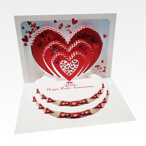 May include: A red and white 3D pop-up card with a layered heart design. The card reads "40th Happy Ruby Anniversary".