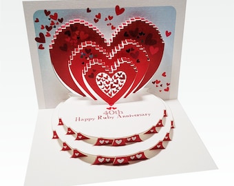 May include: A red and white 3D pop-up card with a layered heart design. The card reads "40th Happy Ruby Anniversary".