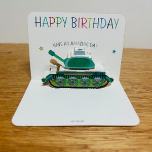 May include: A pop-up birthday card featuring a green tank. The card reads "Happy Birthday" in rainbow colours and "Have an Amazing Day" in black.
