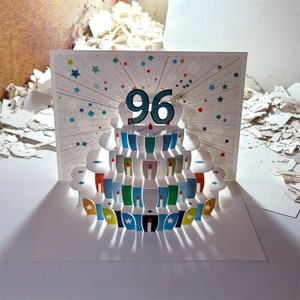 May include: A white pop-up card with a 3D cake design. The cake has 96 candles and is decorated with colorful details. The card is perfect for a 96th birthday celebration.