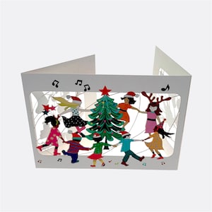 May include: A white card with a pop-up scene of children dancing around a Christmas tree. The children are wearing colourful hats and clothes. The tree is decorated with baubles and lights. There are musical notes around the scene.