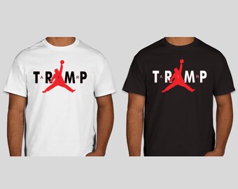 May include: Two short-sleeved t-shirts, one white and one black. Each shirt features the word "TRUMP" in black and white, with a red figure of a person jumping with a basketball.