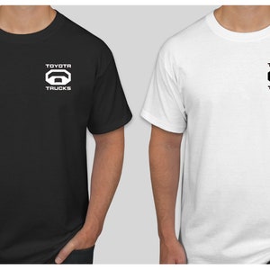 May include: Two t-shirts, one black and one white, with a white logo on the black shirt and a black logo on the white shirt. The logo is a stylized image of a truck with the words "TOYOTA TRUCKS" above it.
