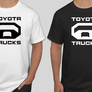 May include: Two t-shirts, one white and one black, each featuring the "TOYOTA TRUCKS" logo in a contrasting color. The logo is a stylized geometric design. The shirts are short-sleeved.