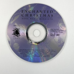 May include: A circular compact disc titled Enchanted Christmas by Anna Maria Mendieta. The disc features a purple background with faint holiday imagery, the Sugo logo, and a tracklist of 15 songs. It includes production details and a 60:05 total time.