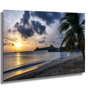 Pode incluir: Uma impressão de praia cênica com um pôr do sol sobre o oceano. O céu está cheio de nuvens escuras e o sol está se pondo sobre a água. Uma palmeira está em primeiro plano e uma pequena ilha ao longe.