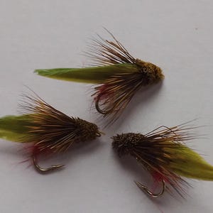 May include: Three brown and green fly fishing lures with red and green feathers.