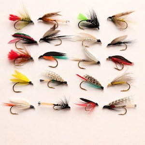 Puede incluir: Una colección de moscas de pesca coloridas con varios diseños de plumas e hilos. Las moscas presentan acentos rojos, amarillos, verdes y marrones, con anzuelos metálicos curvos. Estos señuelos artificiales están diseñados para la pesca con mosca.