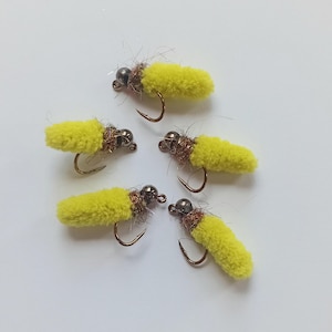 May include: Five yellow fly fishing lures with bronze hooks and dark gray beads. The lures have a fuzzy, cylindrical body and are arranged on a white surface. These artificial flies are designed for catching fish.